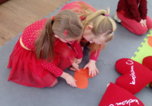 Dwie dziewczynki układają elementy serduszka z papieru w całość.